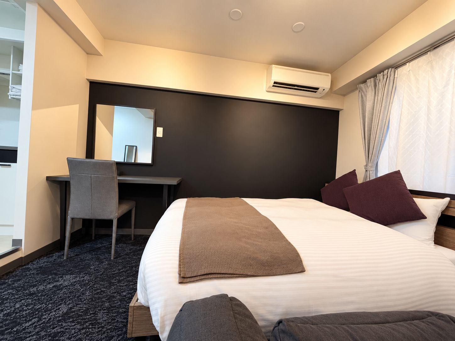 Een hotelkamer met een bed, een bureau, een stoel, een spiegel en een airconditioning.