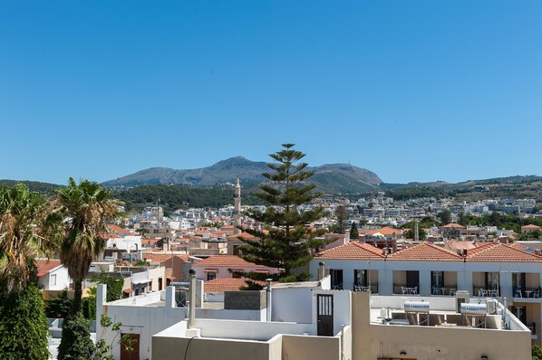 A coastal town with terracotta-roofed buildings, a prominent mosque, and a mountain in the background. - Pallazzo Fortezza (Rethymno)