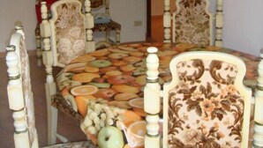Un comedor con una mesa cubierta con un estampado de frutas, rodeada de sillas ornamentadas.