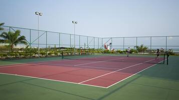 Una cancha de tenis al aire libre con cerca verde, red y cielo despejado.