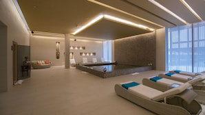 Un espace spa moderne doté d’un jacuzzi, de chaises longues et d’un coin salon avec des coussins.