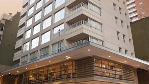 A multi-story hotel with a modern design, featuring a prominent entrance with glass railings and a car parked in front.
