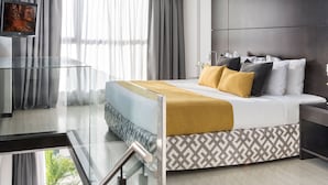 A modern hotel room with a bed, a TV, and a balcony with a glass railing.