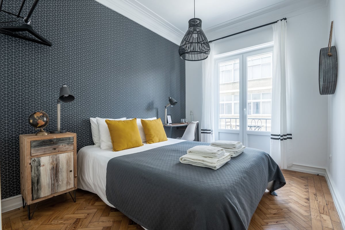 A bedroom with a bed, bedside lamps, a nightstand, and a window with curtains.