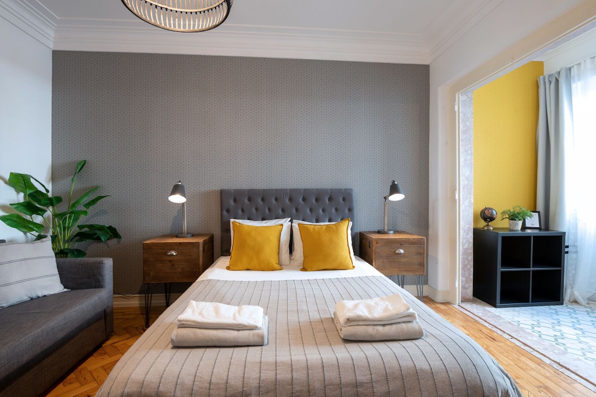 A neatly arranged hotel room with a large bed, two bedside tables, a sofa, and a potted plant.