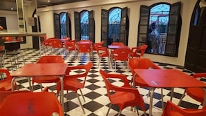Un comedor con sillas y mesas rojas, suelo de cuadros y ventanas grandes con vidrieras decorativas.