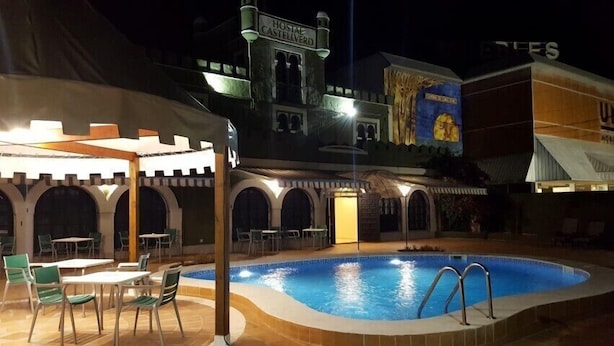 Un patio de hotel con piscina, mobiliario exterior y un mural.