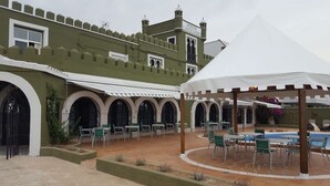 Un patio con piscina, mobiliario exterior y un edificio de fachada que recuerda a un castillo.