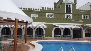 Zona de piscina con un edificio verde que muestra el letrero "Hostal Castellverd" al fondo.