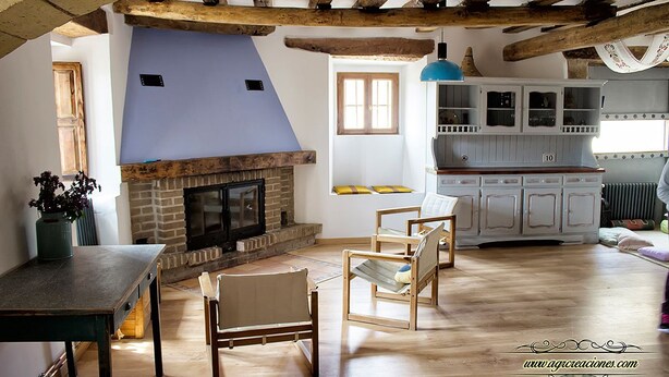 A rustic kitchen with a brick fireplace, wooden beams, and a blue hanging light fixture. - La Madriguera de Tomaso (Valle de Yerri)