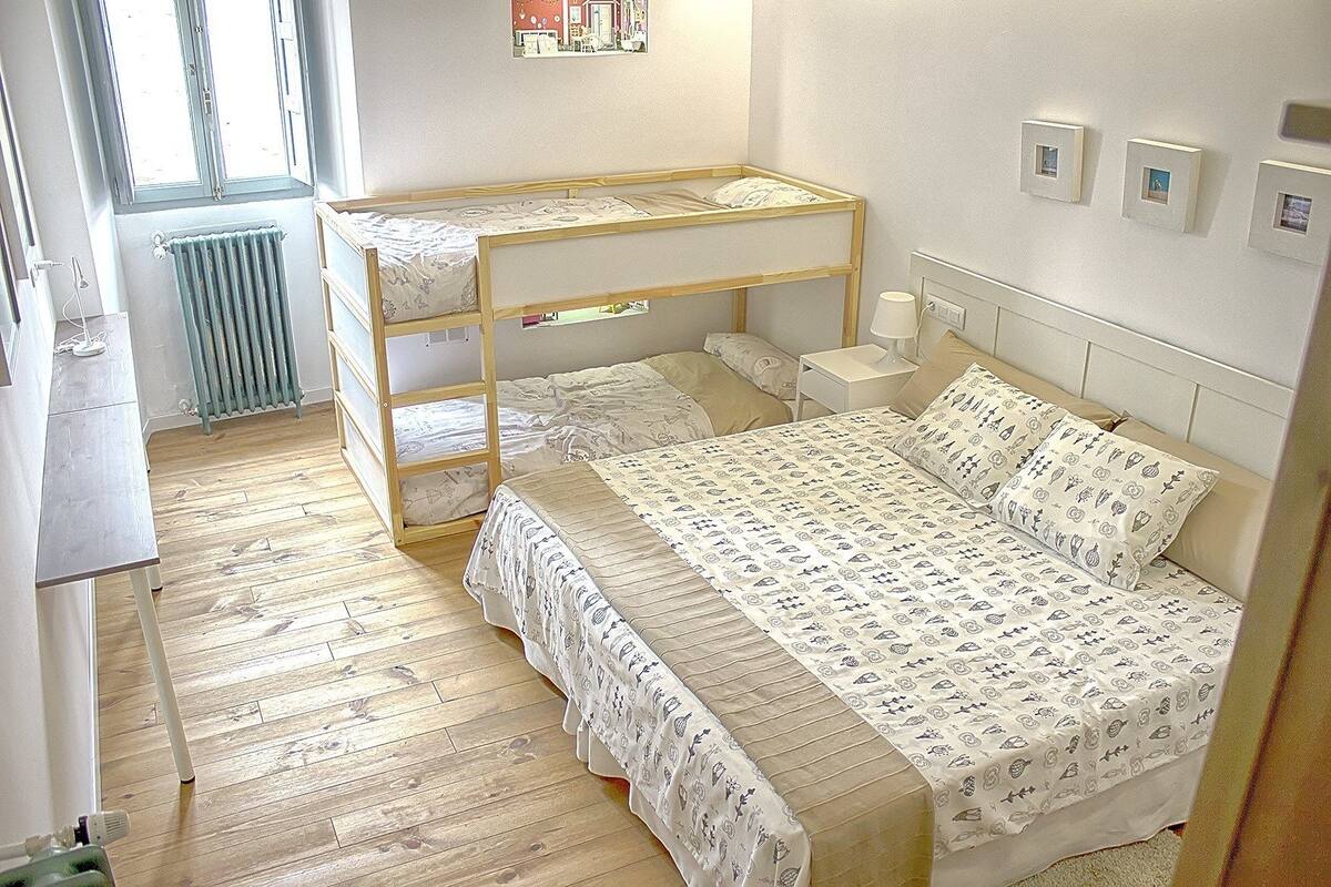 Una stanza con un letto a castello, un letto singolo, un comodino con una lampada e un termosifone.
