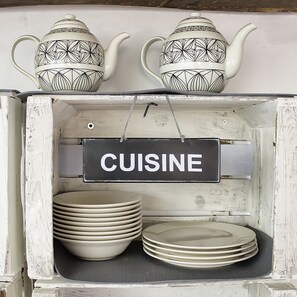 A rustic wooden cabinet with a 'CUISINE' sign, holding stacks of white plates and two patterned teapots. - La Madriguera de Tomaso (Valle de Yerri)