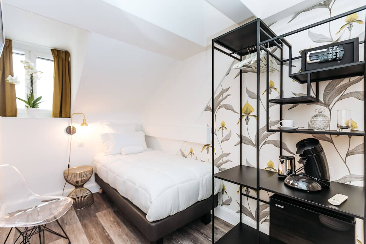 Una habitación de hotel moderna con cama, mesita de noche, silla y escritorio con cafetera.