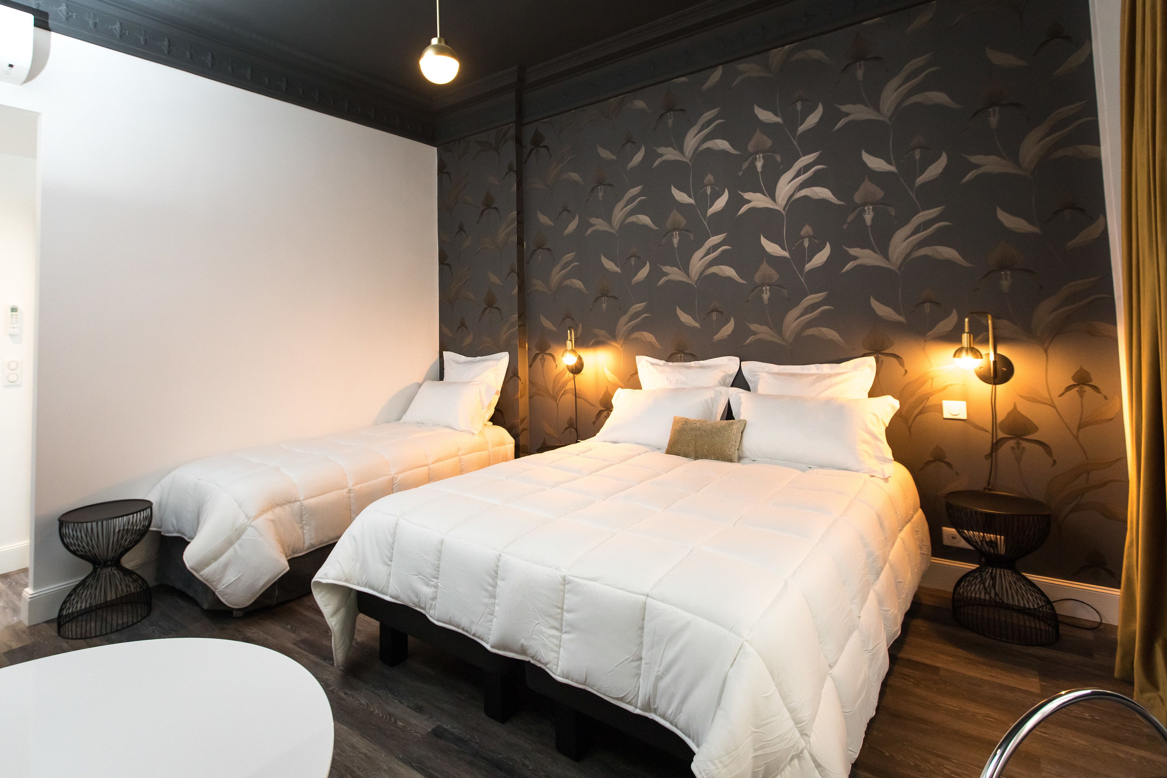 Een hotelkamer met twee bedden, een ronde tafel en een wand met bloemenpatroon.