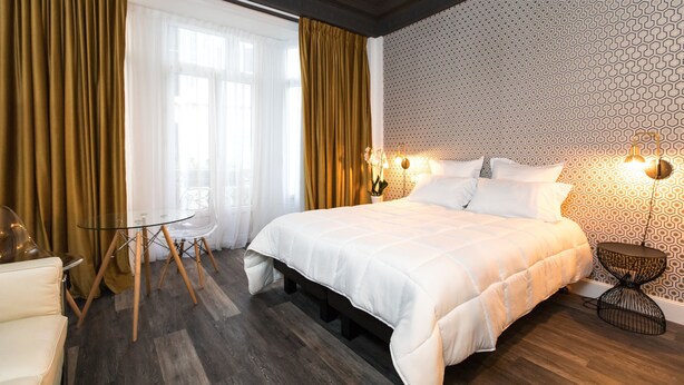 A modern hotel room with a large bed, a glass table, and a patterned wall.