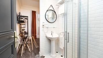 A modern bathroom with a pedestal sink, a glass shower enclosure, and a mirror with a towel hanging on the wall.