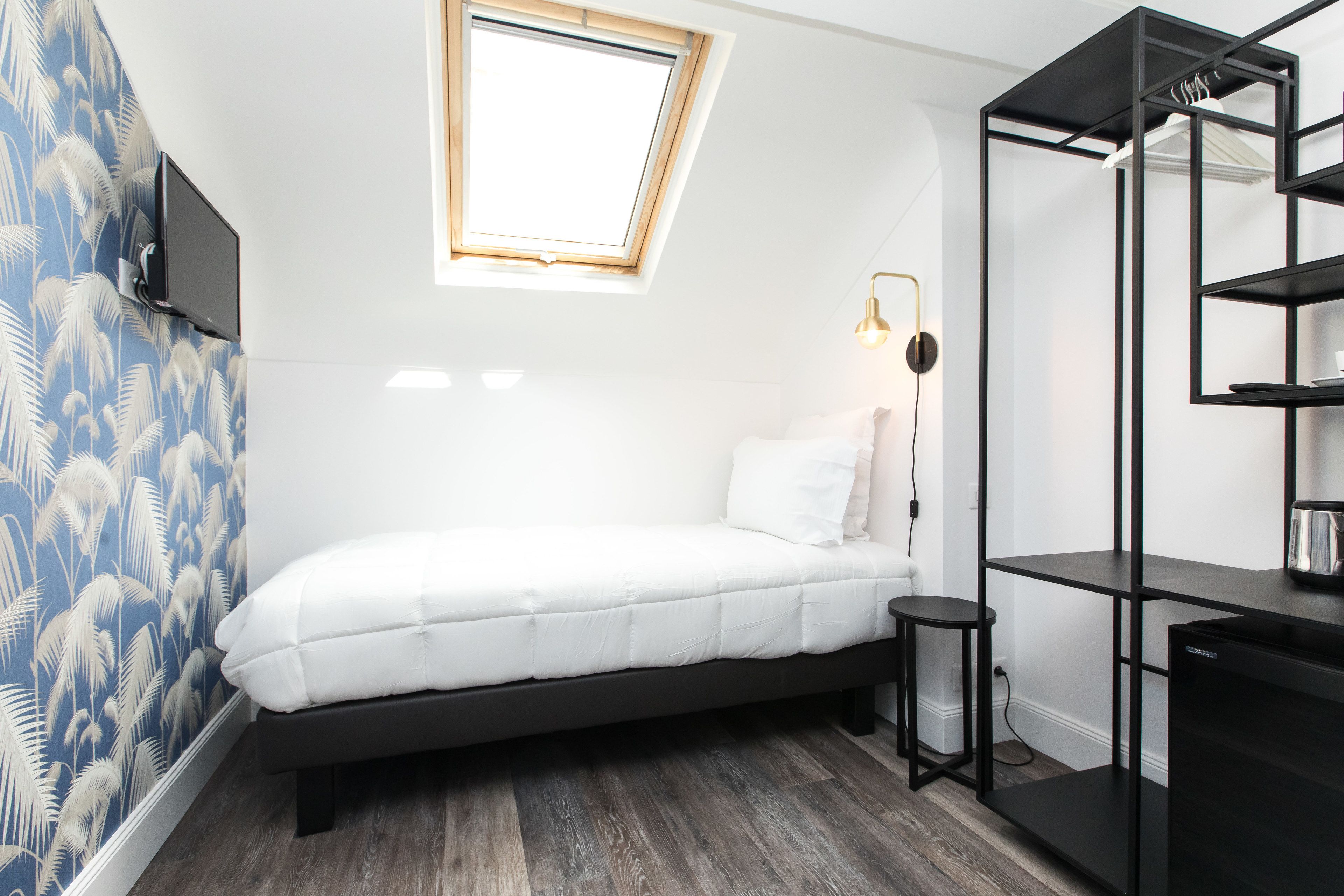 A compact bedroom with a bed, a small stool, a desk, and a shelving unit.