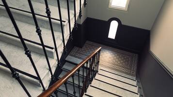 A staircase with black balusters and a wooden handrail, leading to a landing with patterned flooring.