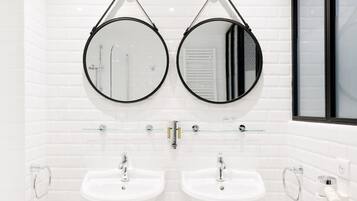 Un baño moderno con dos lavamanos, un inodoro y un bidé, todo en color blanco.