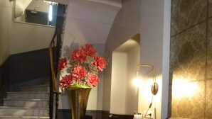 A staircase with a handrail, a table with chairs, a vase of flowers, and a wall-mounted light fixture.