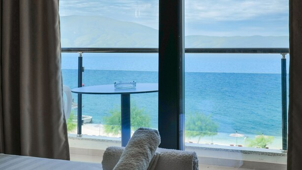 A room with a bed, a table, and a view of the sea. - Hotel Roalb (Orikum)