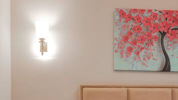 A bedroom with a bed, a nightstand, a wall-mounted light, and a painting of a tree with pink flowers.
