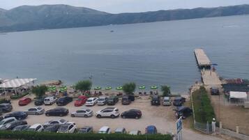 Un parking situé sur la côte, avec des voitures, une jetée et une vue sur la mer et les collines.