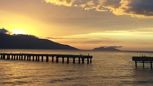 A sunset over a calm body of water with a pier extending into the water. - Hotel Roalb (Orikum)