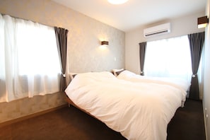 Cama doble en una habitación de hotel con pared estampada, unidad de aire acondicionado y cortinas en las ventanas.