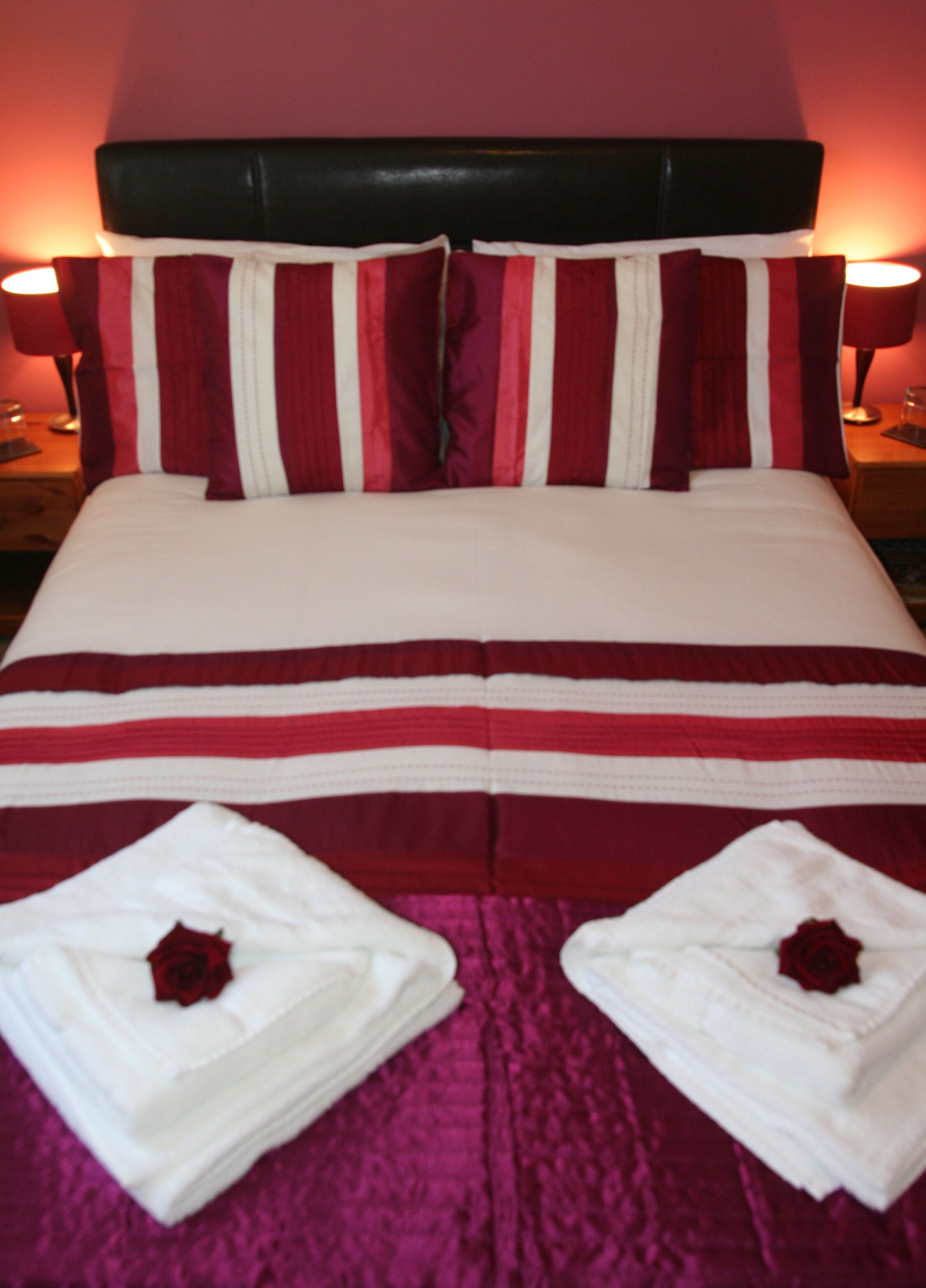 A neatly made bed with striped bedding and two folded towels with rose designs on a purple bedspread.
