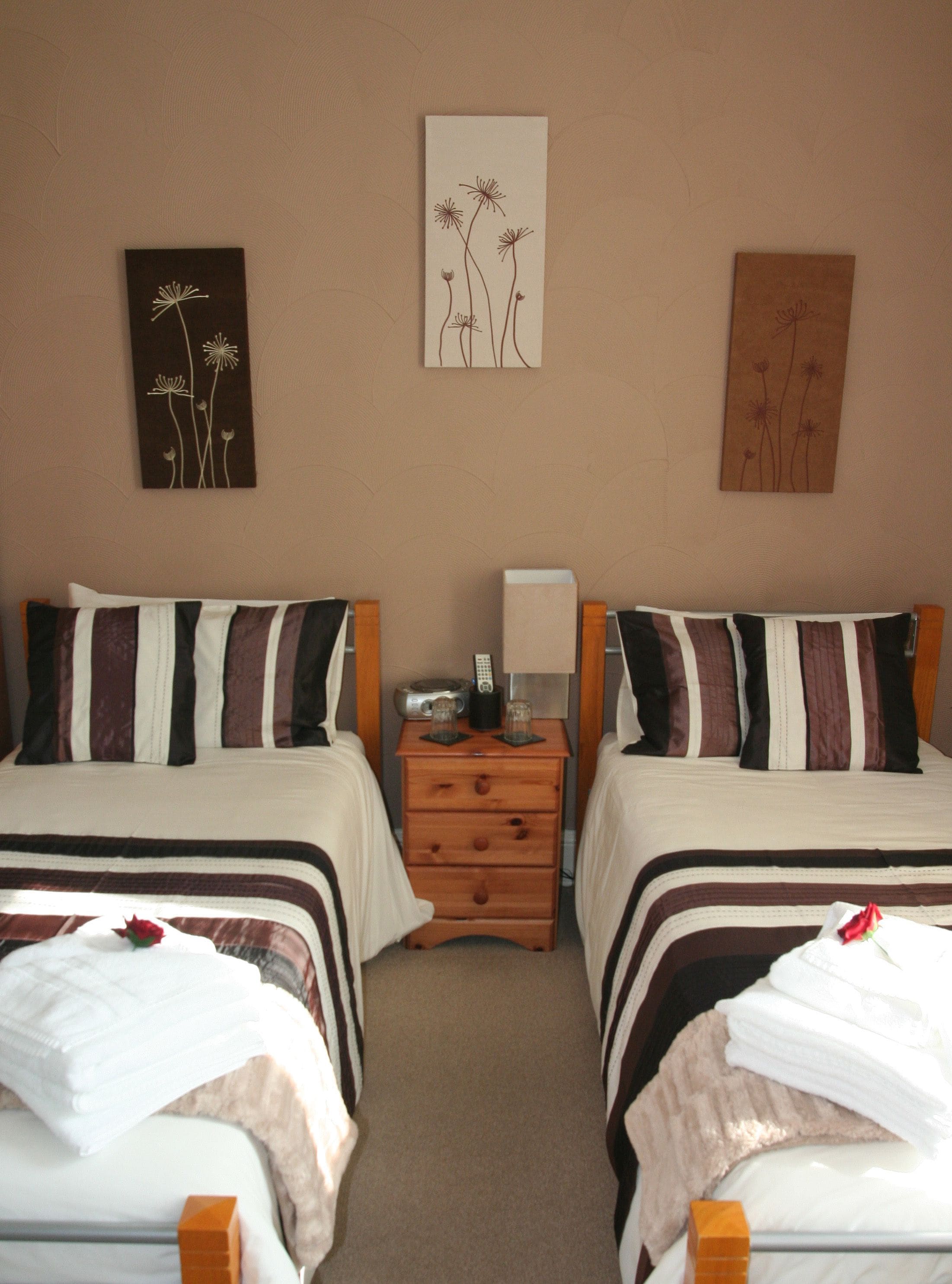 A hotel room with two beds, a nightstand with a lamp, a remote control, and a small table with glasses.
