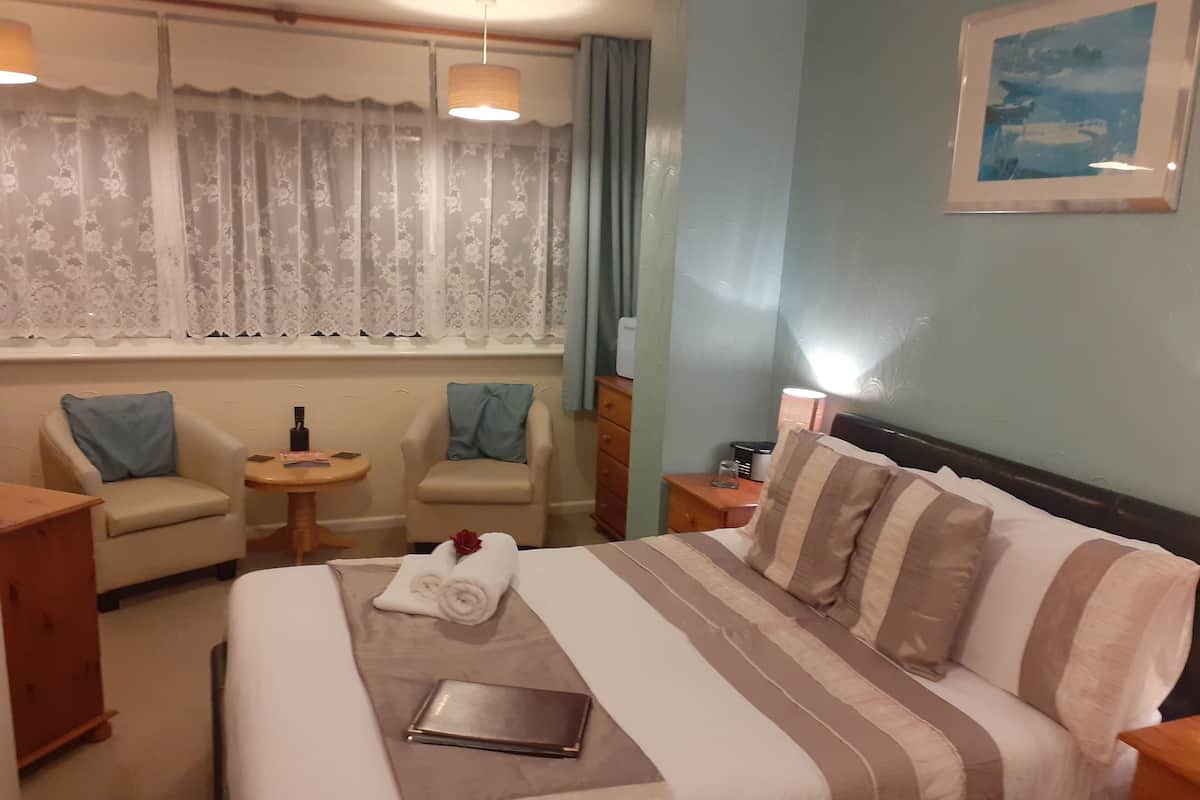 Een hotelkamer met een bed, twee fauteuils, een tafeltje, een lamp en een raam met gordijnen.