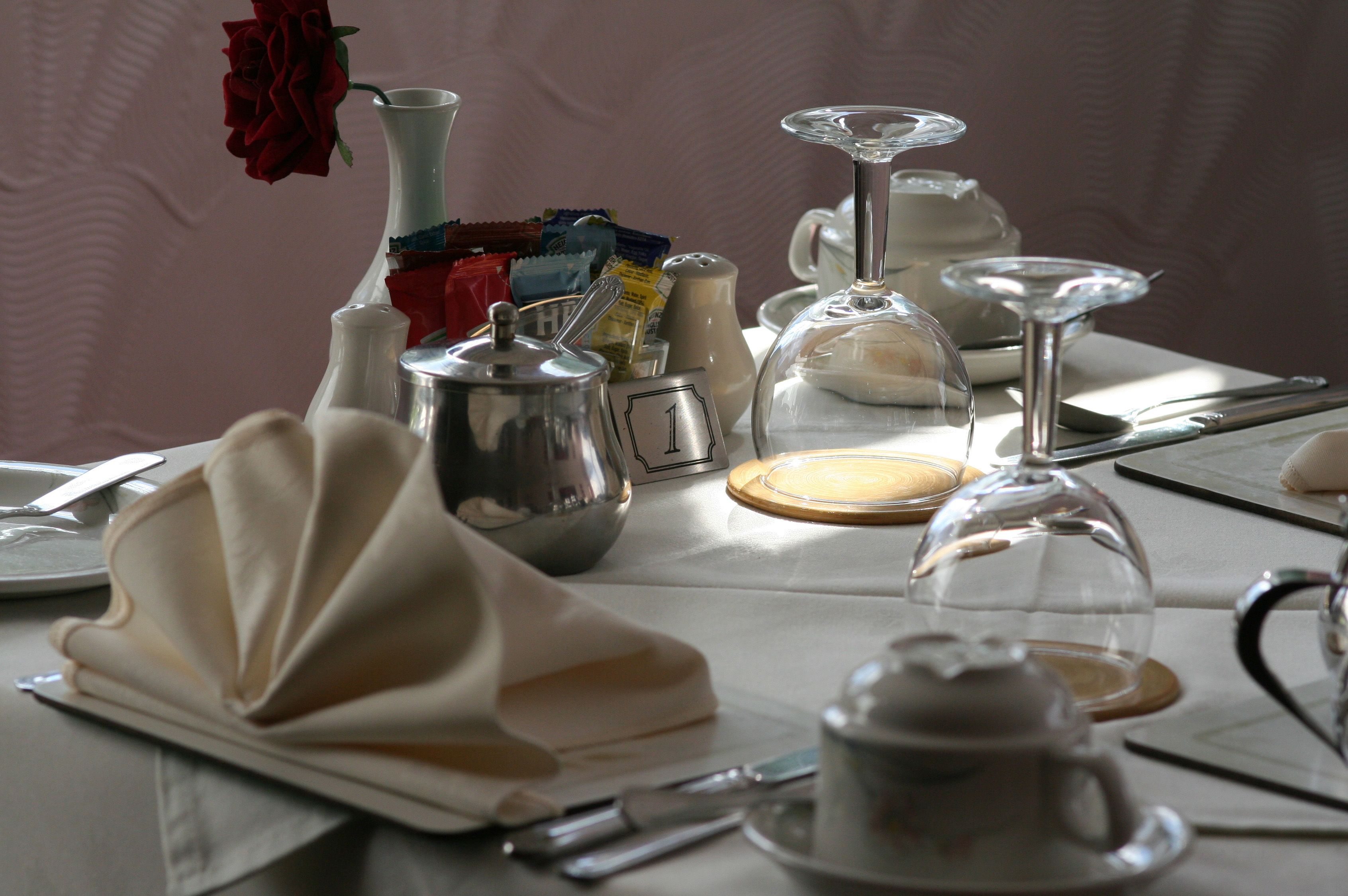 A table set with a teapot, sugar cubes, a glass, and a vase with a red rose.