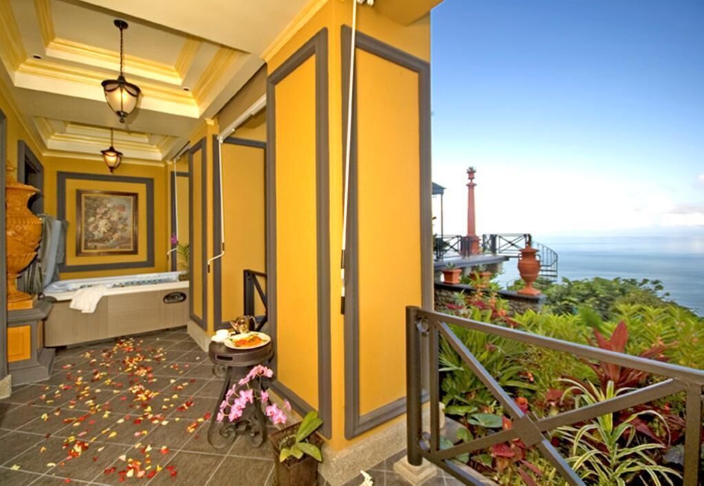 A hotel corridor with a view of the ocean, a balcony with plants, and a decorative vase.