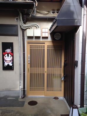 A traditional Japanese entrance with a wooden door, a small window, and a sign above the door.