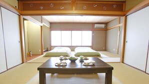 Ein traditioneller japanischer Raum mit Tatami-Böden, einem niedrigen Holztisch mit grüner Sitzauflage und zwei Tatami-Matten mit Kissen.