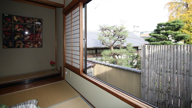 Ein traditioneller japanischer Raum mit Tatami-Böden, Shoji-Schirmen und Blick auf einen Bambuszaun sowie Bäume.