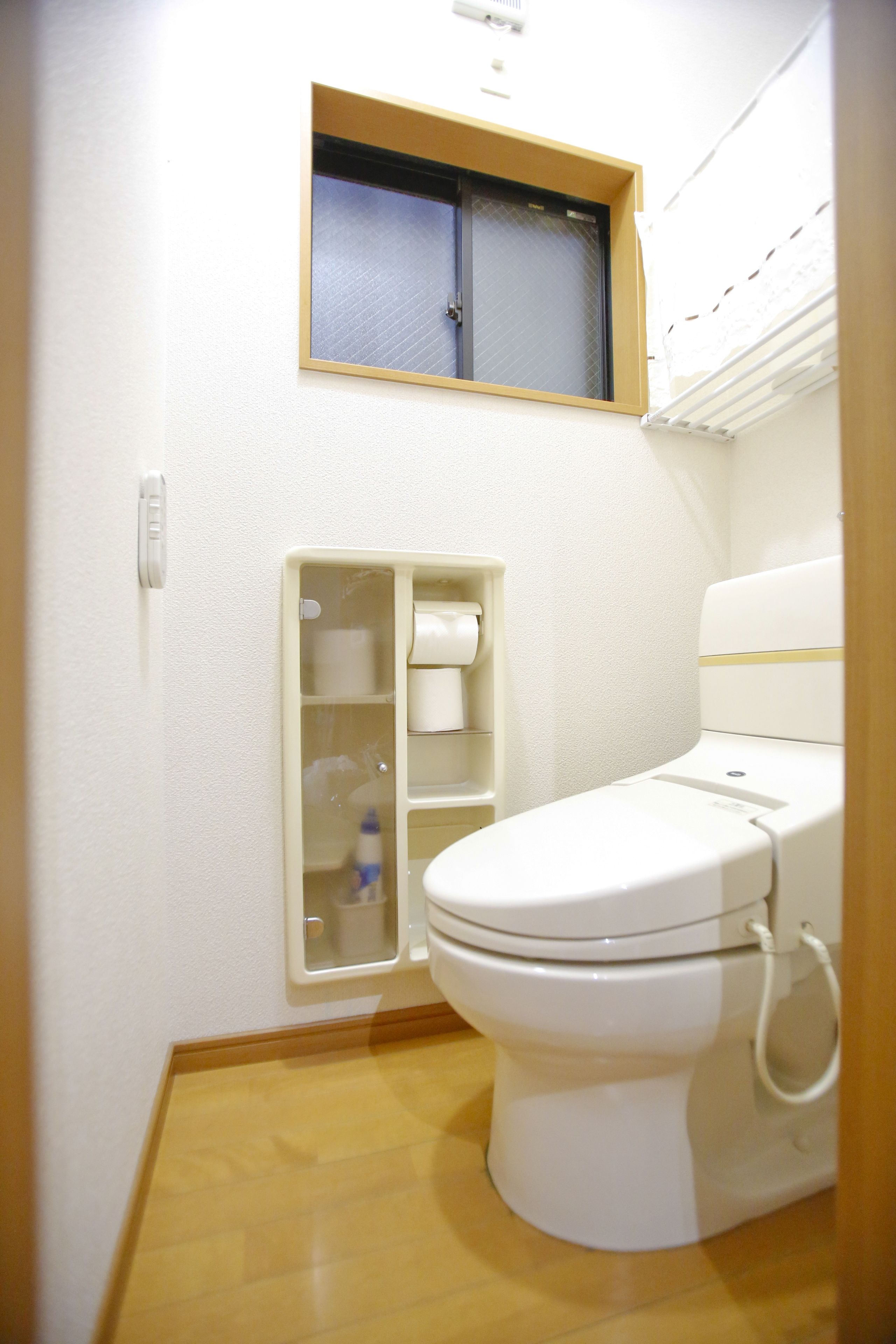 Une petite salle de bain compacte, équipée de toilettes, d’une fenêtre et d’une étagère où sont rangés les articles de toilette.