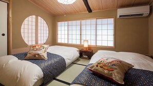 A traditional Japanese-style room with tatami flooring, two beds with patterned bedding, a shoji screen window, and a ceiling fan. - Private Residence Nijo-jo Nagomi (Kyoto)