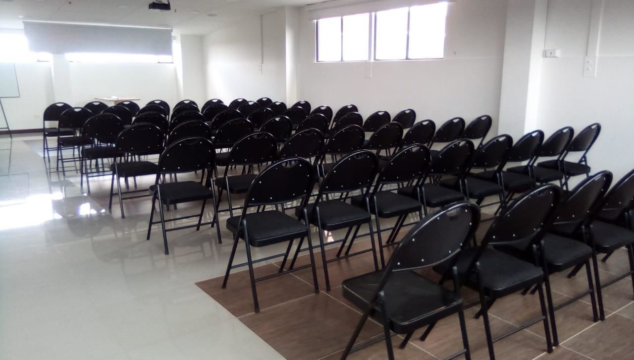 Une salle de conférence avec des rangées de chaises noires, un tableau blanc et un projecteur.
