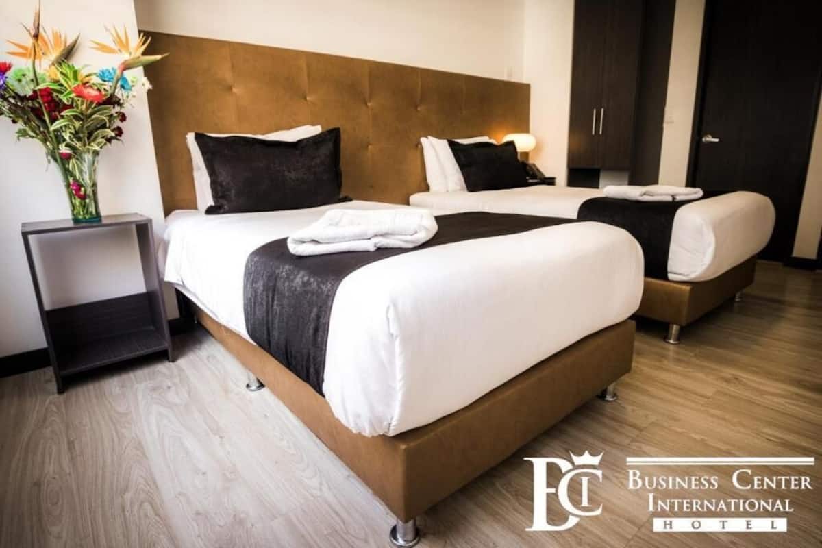 A hotel room with two beds, a wooden headboard, a nightstand, and a vase of flowers.