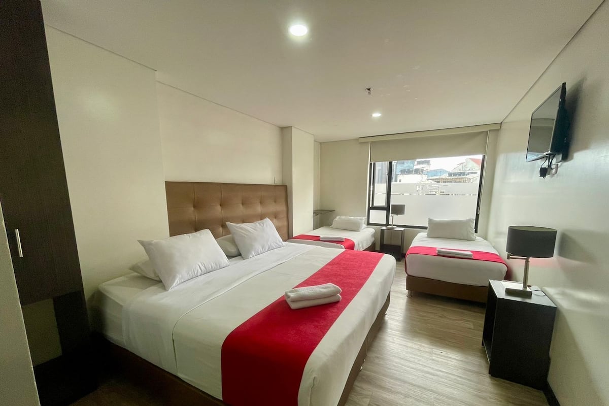 A hotel room with two beds, a large window, a flat-screen TV, and a desk with a lamp.
