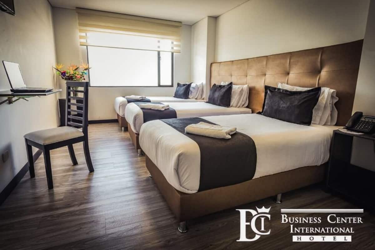 A hotel room with two beds, a desk with a laptop, a chair, and a bedside table with a phone.