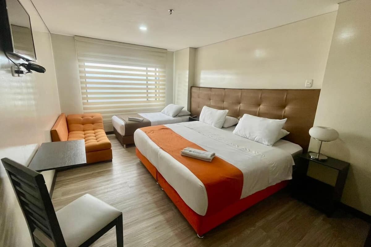 A hotel room with a large bed, a sofa, a desk, and a chair.