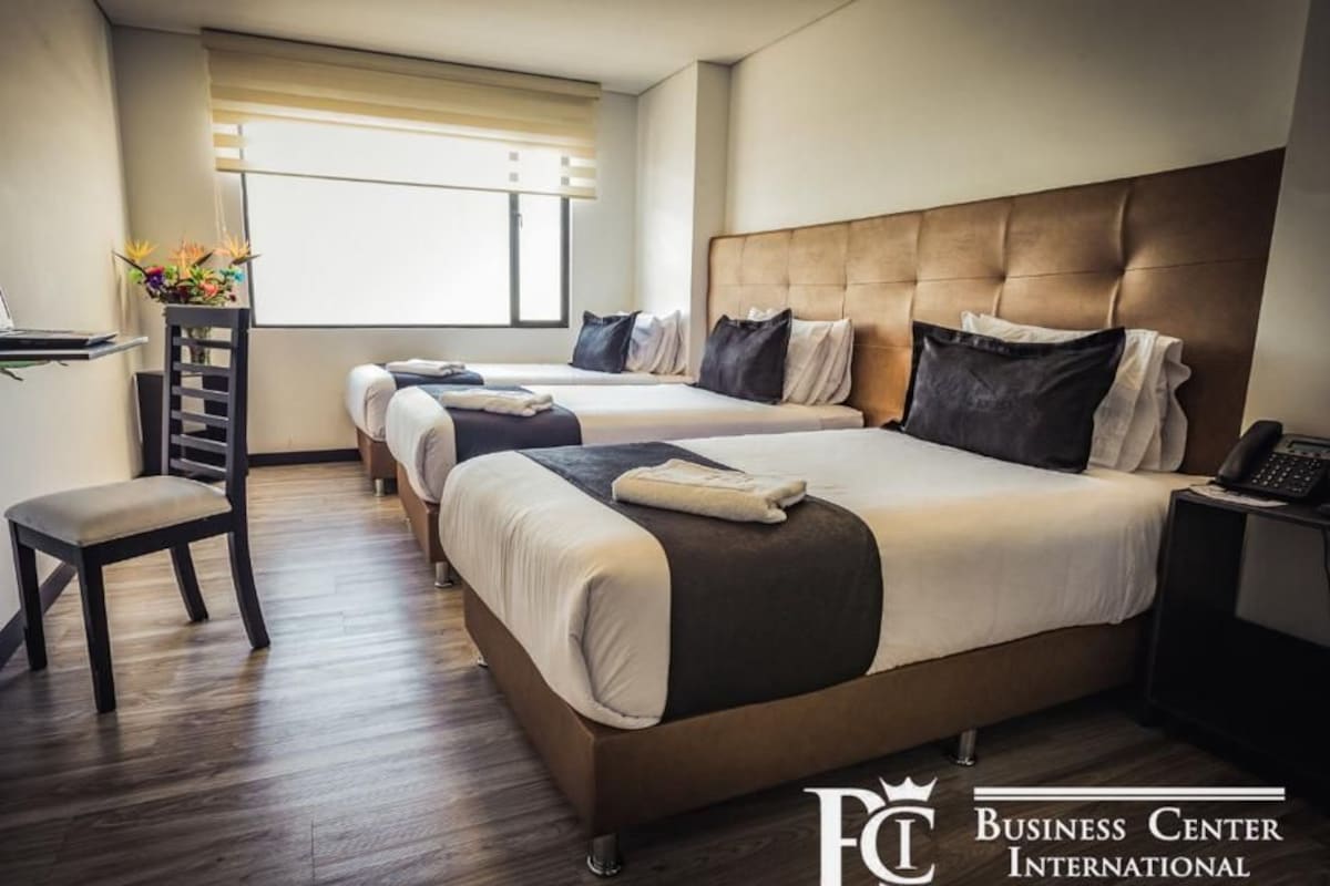 A hotel room with two beds, a desk with a laptop, a chair, and a bedside table with a phone.