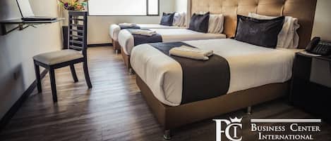 A hotel room with two beds, a desk with a laptop, a chair, and a bedside table with a phone.