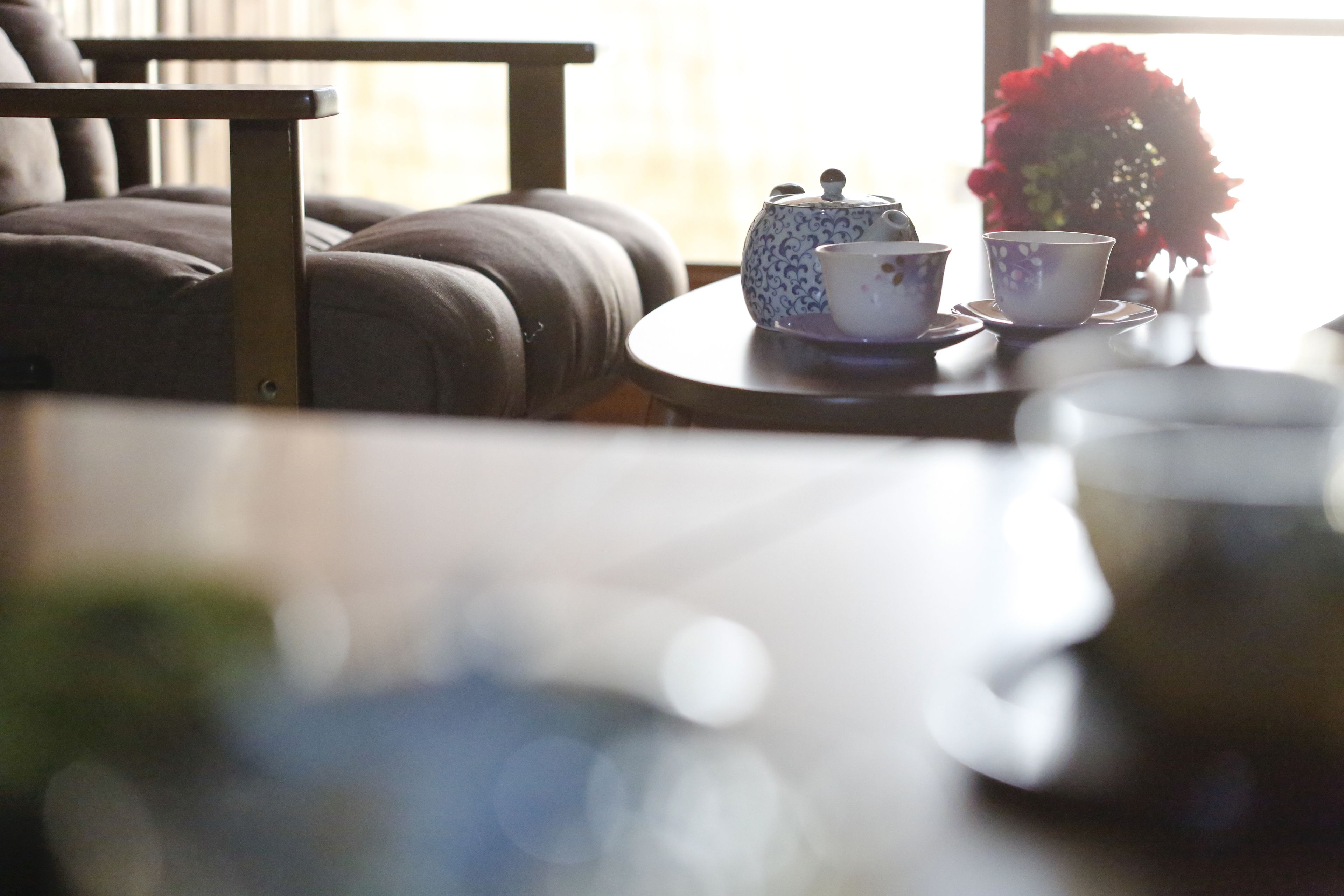 A cozy seating area with a table set for tea, a vase with flowers, and a window with natural light.