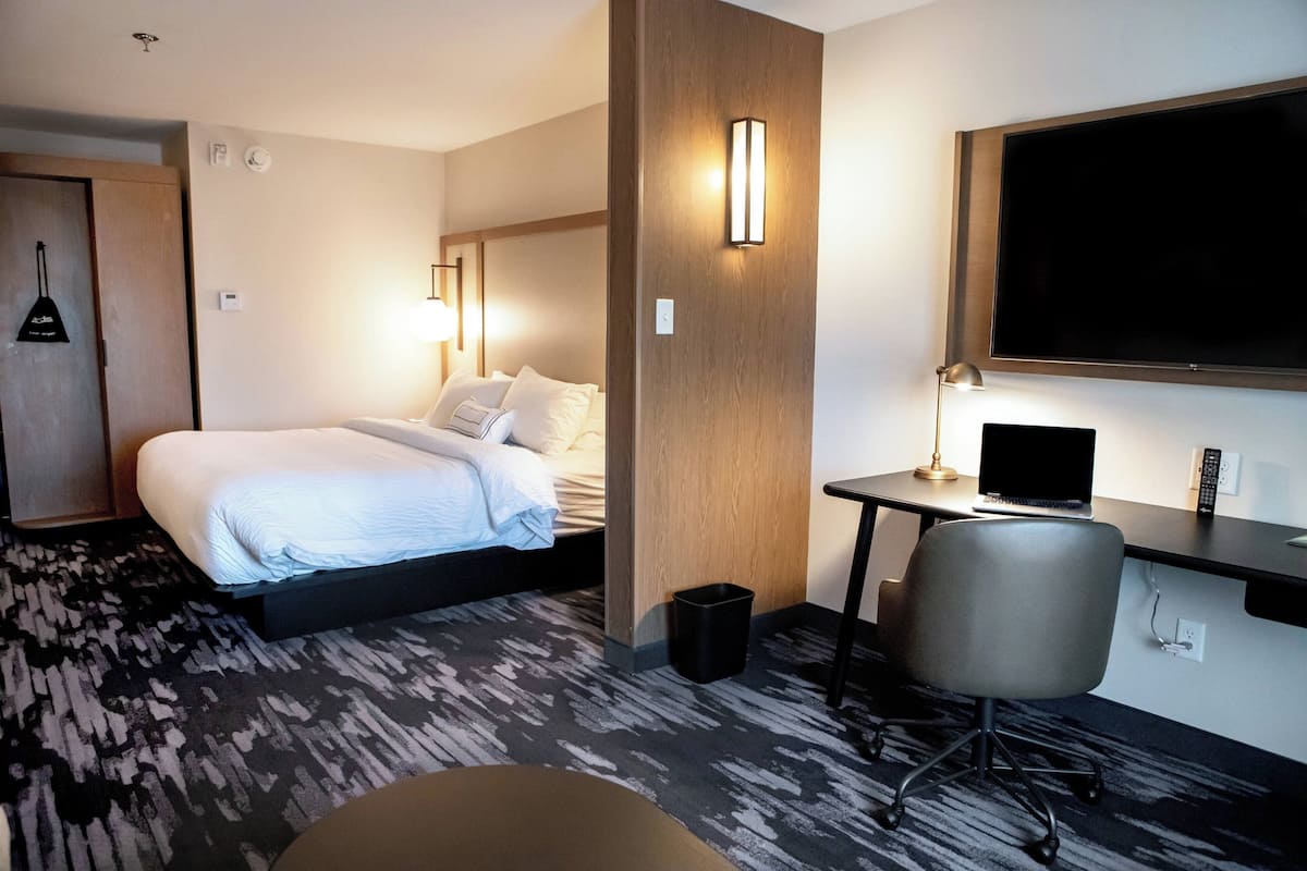 A hotel room with a bed, desk, chair, TV, and a trash bin.