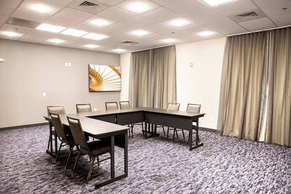 Une salle de conférence avec une grande table, des chaises, un tableau au mur et des rideaux.
