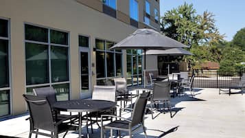 An outdoor patio with tables and chairs, large windows, and a covered seating area.